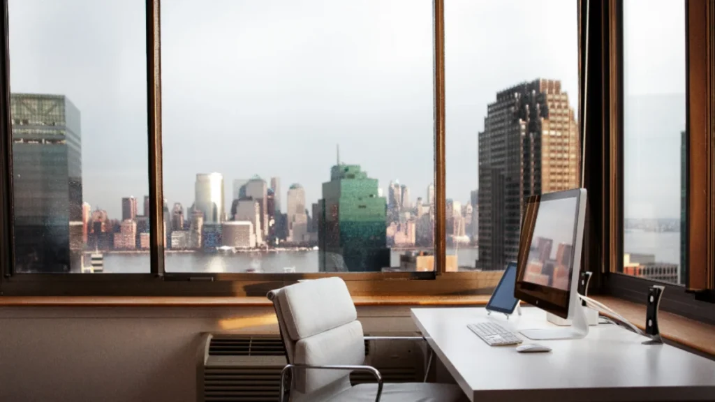 Escritório moderno e organizado com mesa de trabalho, computador e vista urbana ao fundo